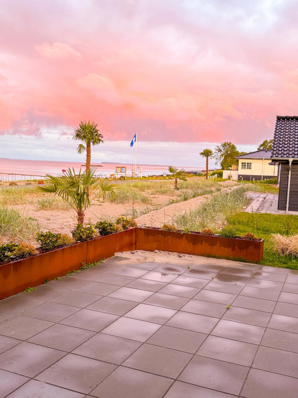 Palmer ved stranden i solnedgang med terrasse og plantekasser i cortenstål